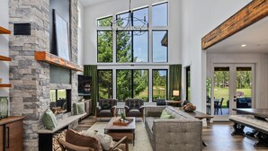 A spacious living room with a stone fireplace, large windows, and a view of the outdoors. - Suncadia's Best Kept Secret | Experience Luxury @ Great Rates (Cle Elum)