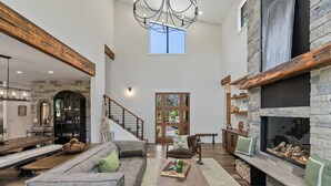 A spacious living area with a stone fireplace, a wooden ceiling beam, and a staircase leading to an upper level. - Suncadia's Best Kept Secret | Experience Luxury @ Great Rates (Cle Elum)