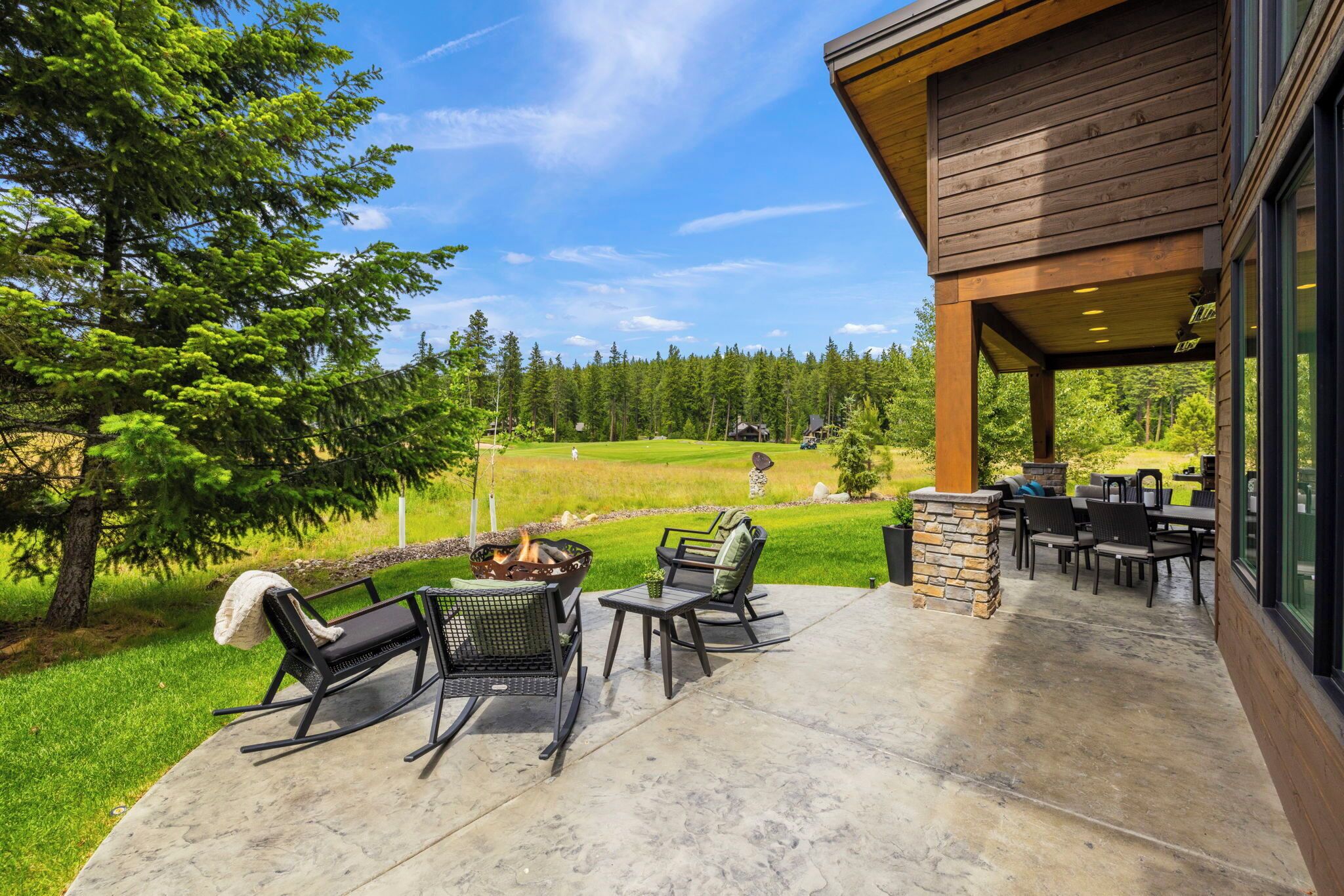 Un patio cubierto con mobiliario exterior, una fogata y vistas a un campo de golf.