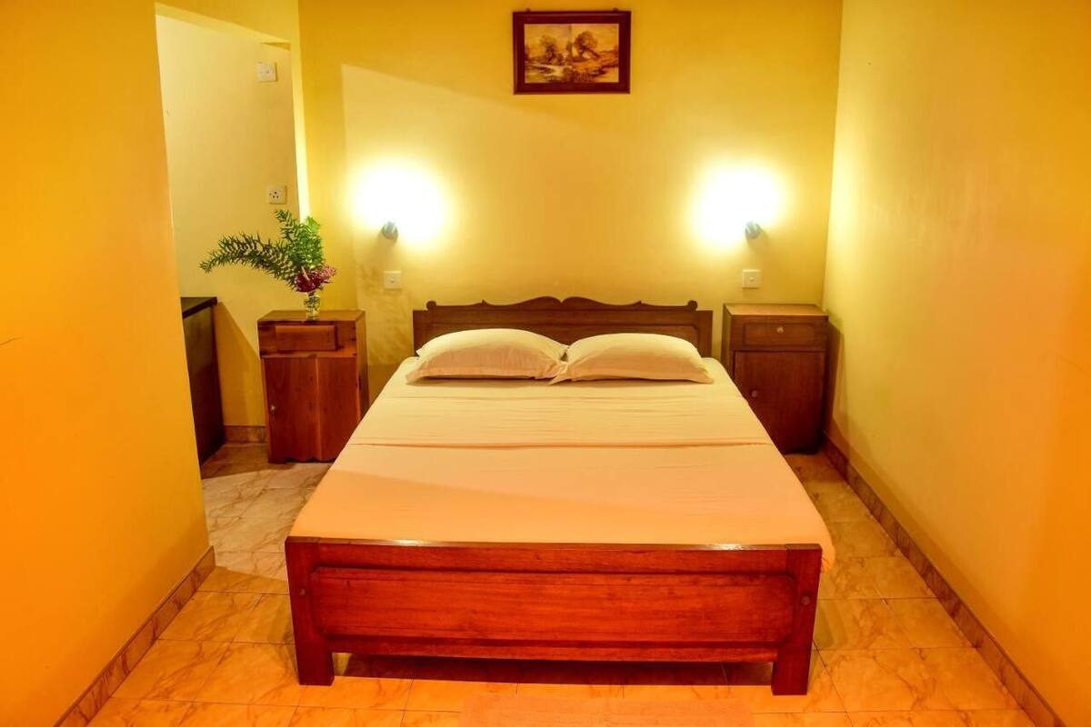 A neatly made bed in a room with yellow walls, two bedside tables, and a framed picture above the bed.