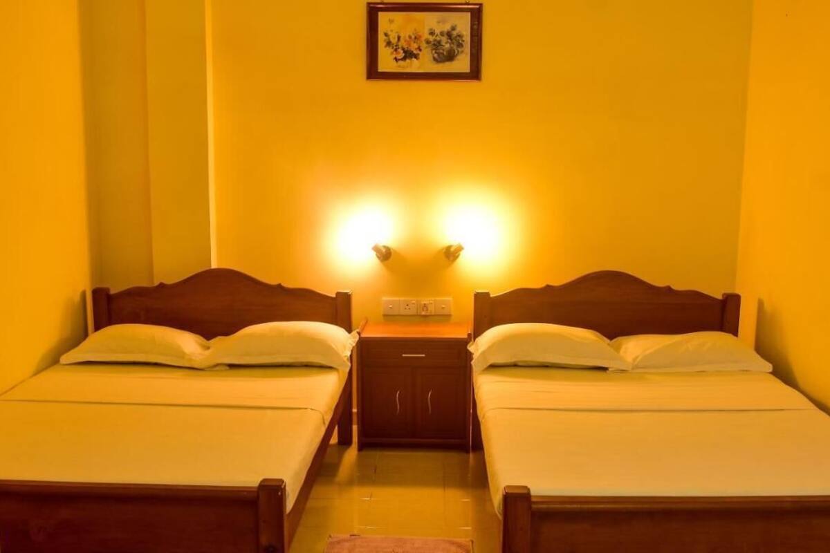 A room with two single beds, a nightstand with a lamp, and a wall-mounted picture.