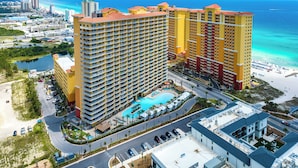 A high-rise hotel with multiple balconies, a swimming pool, and a beach view.