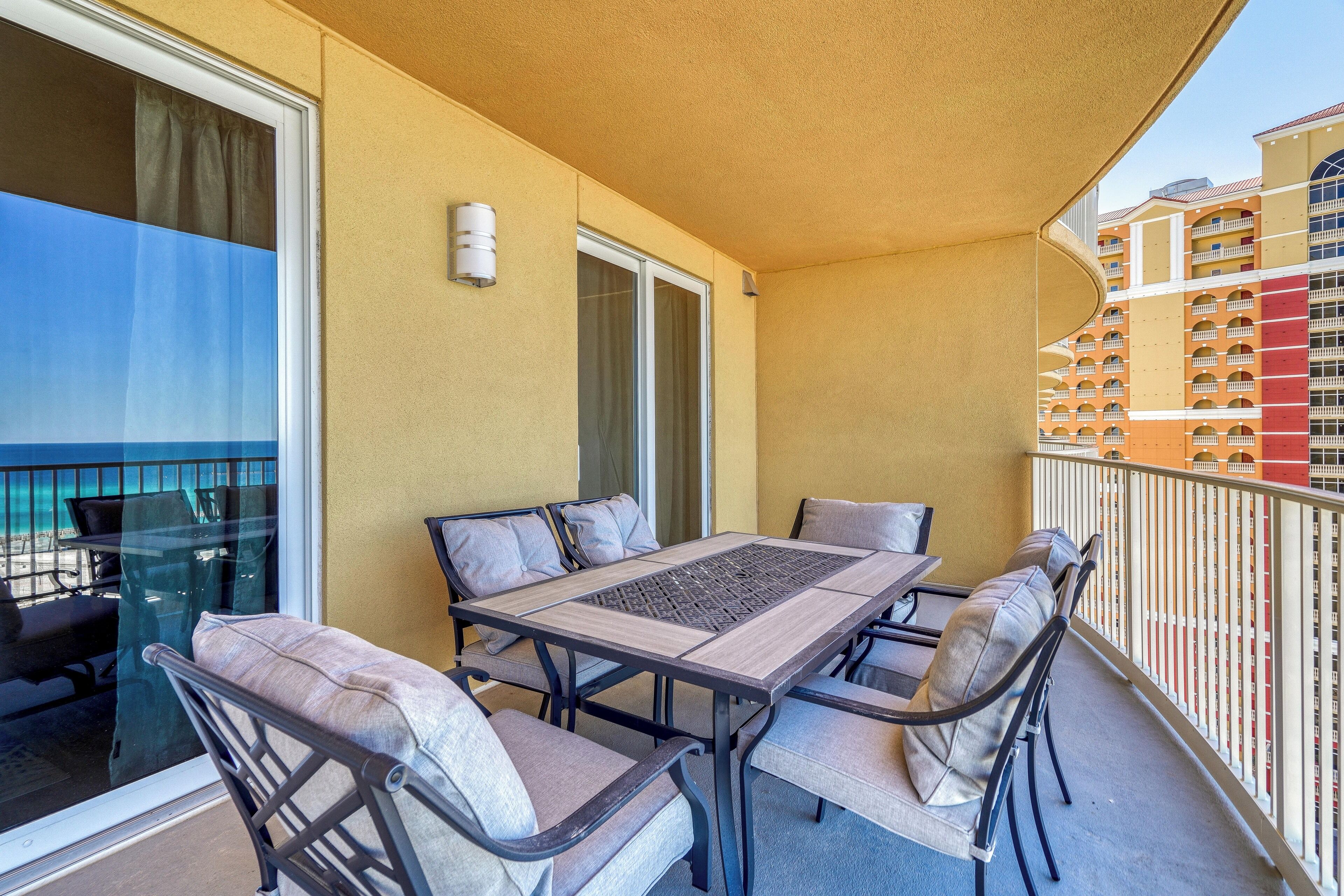 En balkon med et bord og stole, en skydedør samt udsigt til en bygning med altaner.