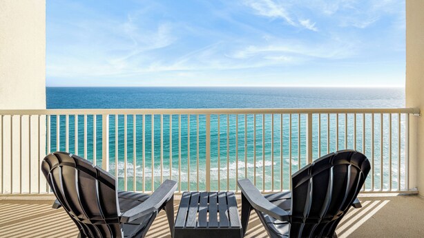 Un balcon avec deux fauteuils Adirondack et une petite table, donnant sur un océan bleu et limpide, avec une balustrade blanche.