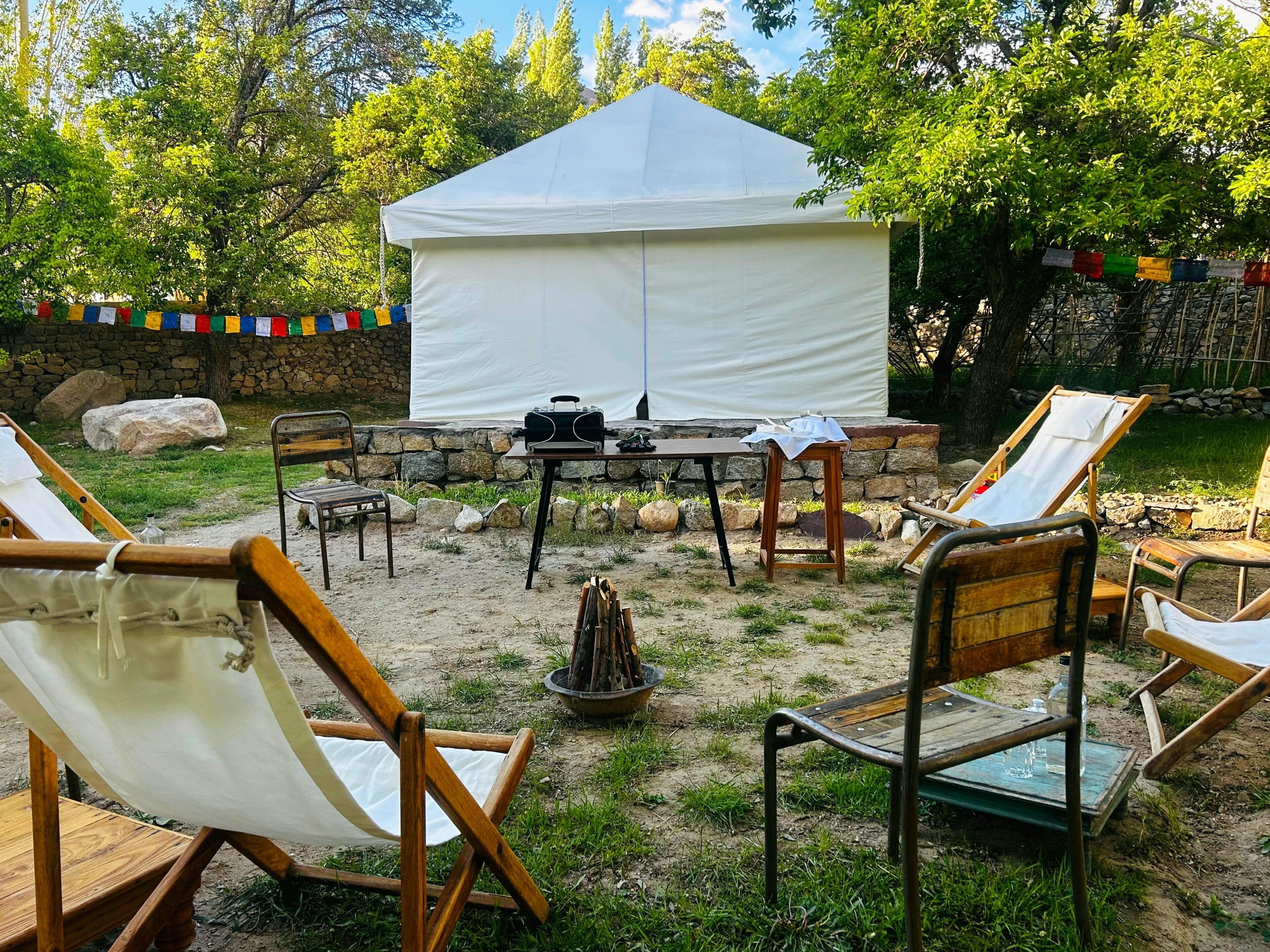 A tented outdoor area with lounge chairs and a table, surrounded by greenery and stone walls.