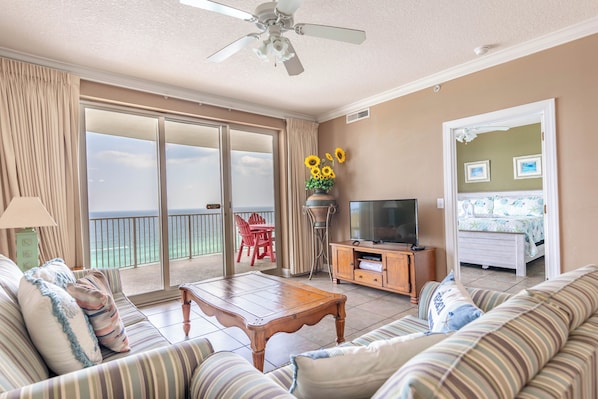 A living room with a sofa, a coffee table, a TV, and a balcony with a view. - BIG Beachfront Balcony and New Furnishings (Panama City Beach)