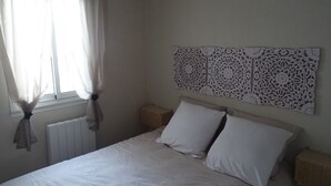A bedroom with a bed, white curtains, a woven headboard, and a radiator. - la Castagna (San-Nicolao)