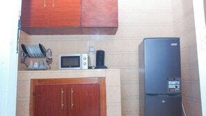 A compact kitchen with wooden cabinets, a microwave, and a black refrigerator. - Appartement Meublé à Keur Massar, Dakar Sénégal. Proche Lac Rose et Aéroport (Keur Massar)