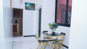 A dining area with a table and chairs, a potted plant, and a view through a window. - Appartement Meublé à Keur Massar, Dakar Sénégal. Proche Lac Rose et Aéroport (Keur Massar)