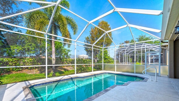 Une piscine entourée d’une structure en verre, elle-même bordée d’un jardin et d’arbres.