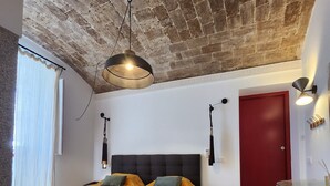 A room with a brick ceiling, two beds with matching headboards, a red door, and a small table with a vase.