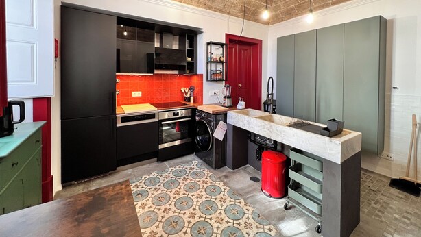 A modern kitchen with black cabinets, a red door, and a marble countertop.
