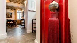 A hallway with a red door, a hanging lamp, and a staircase leading to another room.