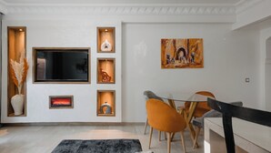 Un salon moderne doté d’un téléviseur à écran plat, d’étagères décoratives, d’une cheminée et d’un coin repas avec des chaises orange.