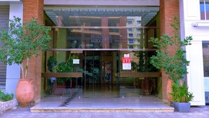 L’entrée d’un hôtel, avec des portes en verre, une façade en briques et des plantes en pot de chaque côté.