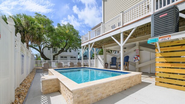 Une piscine avec une terrasse en bois, un espace extérieur aménagé et couvert, et une clôture blanche.