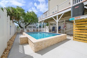 Une piscine avec une terrasse en bois, un espace extérieur aménagé et couvert, et une clôture blanche.