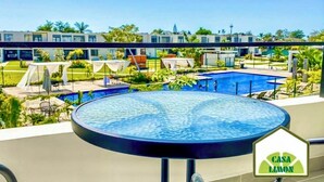 Un espace piscine doté d’un jacuzzi circulaire, de chaises longues et de parasols. On aperçoit des bâtiments modernes en arrière-plan.