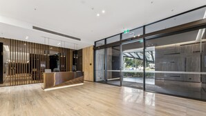 A modern reception area with a wooden reception desk, glass doors leading outside, and a polished marble floor. - Mega Style Apartments Kings Domain (Southbank)
