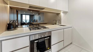 A modern kitchen with white cabinetry, a stainless steel range, and a built-in oven. - Mega Style Apartments Kings Domain (Southbank)
