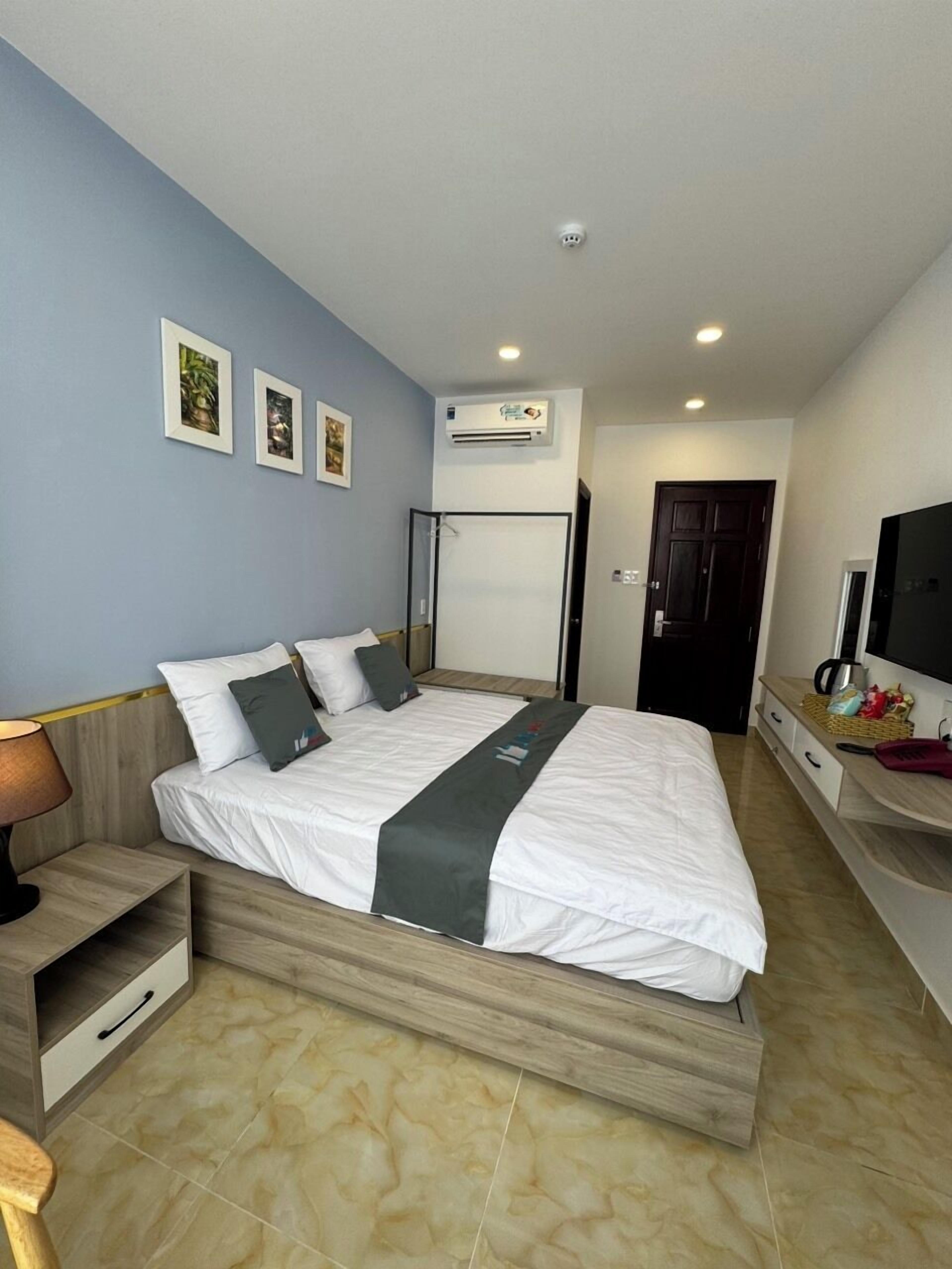 A modern bedroom with a bed, bedside tables, a TV, and an air conditioning unit.
