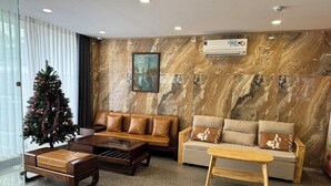 Un hall d’entrée moderne avec un mur de marbre, des canapés en cuir, une table basse en bois et un sapin de Noël.