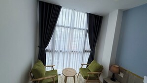 Une pièce avec deux fauteuils verts, une petite table ronde, une lampe et une fenêtre ornée de rideaux légers.