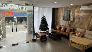 Un hall d’hôtel moderne avec une entrée en verre, un sapin de Noël, des canapés en cuir et un mur en marbre.