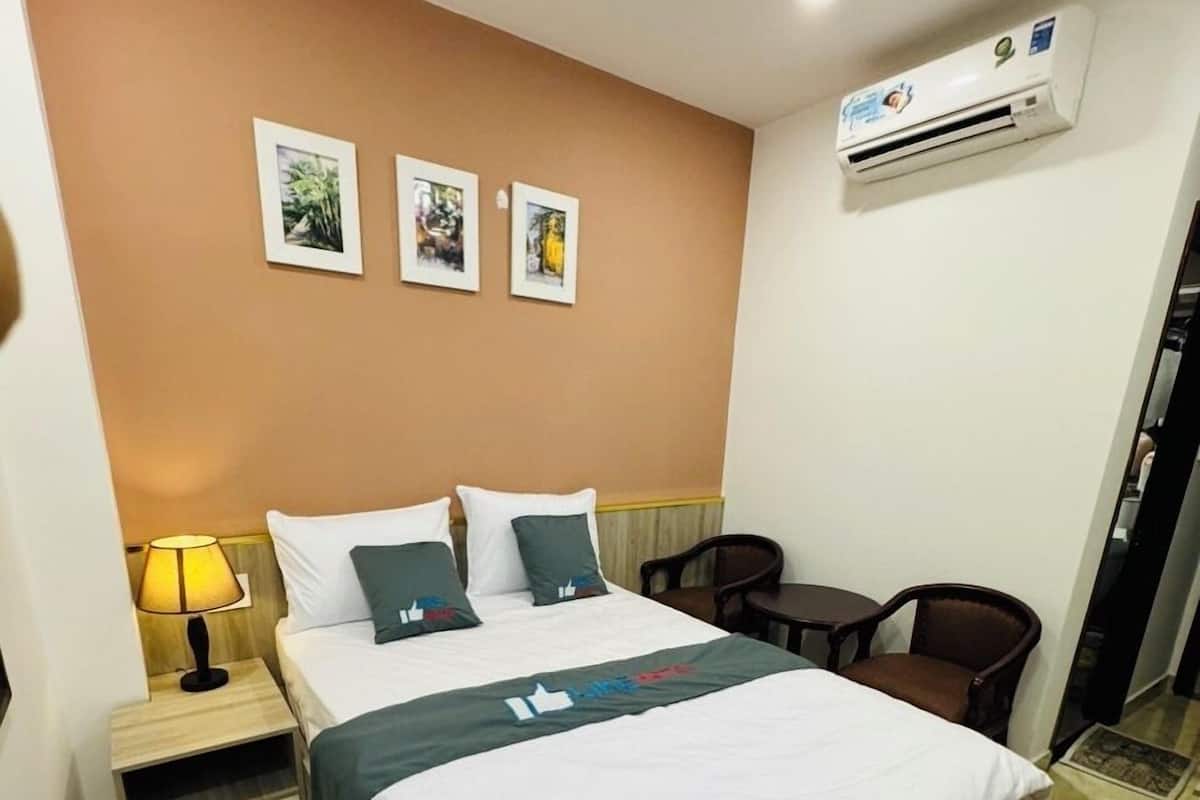 A hotel room with a bed, a nightstand, a chair, and an air conditioning unit.