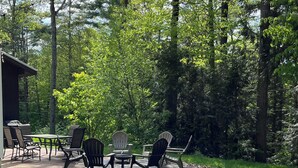 An outdoor patio with a table and chairs, surrounded by trees. - Spectacular kid friendly home 2 minutes to Luzerne beach, 10min to Lake George! (Lake Luzerne)