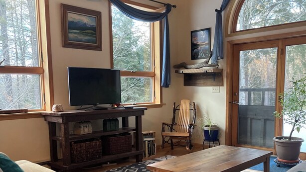 A cozy living room with a wooden ceiling, a television on a wooden stand, a patterned rug, and two sofas. - Spectacular kid friendly home 2 minutes to Luzerne beach, 10min to Lake George! (Lake Luzerne)