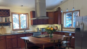 A kitchen with a central island, wooden cabinets, a stainless steel range hood, and a large window providing natural light. - Spectacular kid friendly home 2 minutes to Luzerne beach, 10min to Lake George! (Lake Luzerne)