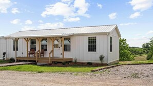 A white building with a porch, wooden chairs, and a gravel driveway.