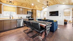 A modern kitchen with wooden ceiling, stainless steel appliances, and a dining area with a table and chairs.