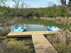A wooden dock extending into a calm pond with two blue boats moored at the end.