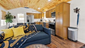 A cozy living room with a sofa and a coffee table, a kitchen with wooden cabinets and appliances, and a ceiling with wooden beams.