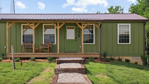 A green single-story house with a porch, two windows, and a door.