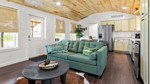 Amplia sala de estar con un sofá verde, una mesa de centro y una zona de cocina con armarios de color claro y electrodomésticos modernos.