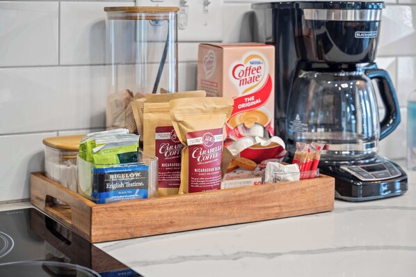 A kitchen counter with coffee-making supplies, including a coffee maker, bags of coffee, and a box of coffee creamer.