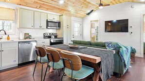 A modern kitchen with wooden ceiling, white cabinets, stainless steel appliances, and a dining area with a green sofa and wooden chairs.