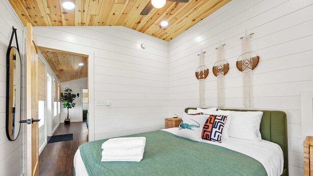 A hotel room with a wooden ceiling, a bed with a green bedspread, white bedding, and decorative wall hangings.