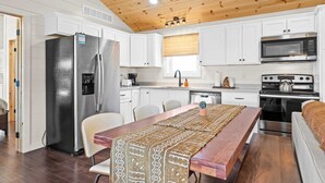 A modern kitchen with white cabinets, stainless steel appliances, and a wooden ceiling.