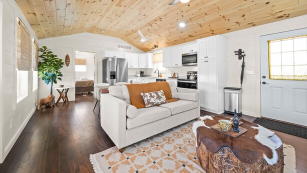 A spacious living area with a wooden ceiling, a white sofa, a dining table, and a kitchen in the background.