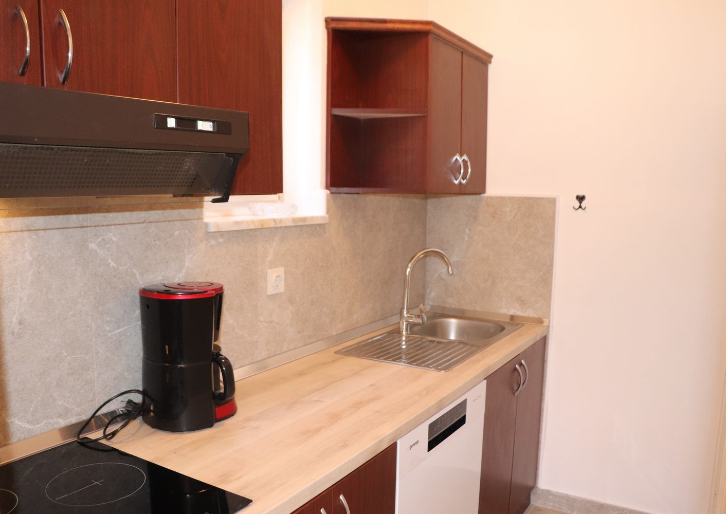 A compact kitchen with a built-in stove, a coffee maker, a sink, and wooden cabinets.