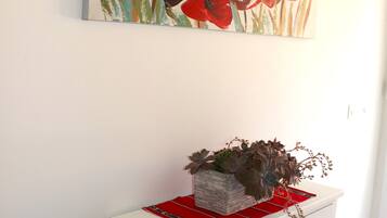 A white cabinet with black knobs, a red tray, and a floral painting above it.