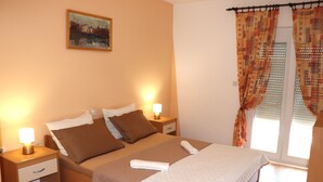 A hotel room with a bed, bedside tables, a painting on the wall, and curtains on the window. - Apartment mit Meerblick (Barbat)