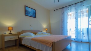 Une chambre à coucher avec un lit en bois, deux tables de chevet avec des lampes, une petite table d’appoint, un tableau au mur et des rideaux légers à motifs floraux.