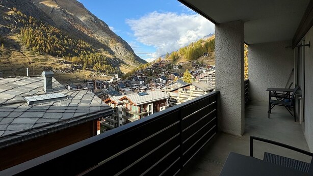 A balcony with a view of a mountainous town, featuring a mix of residential buildings and a prominent mountain peak. - Apartment Hirle (Zermatt)