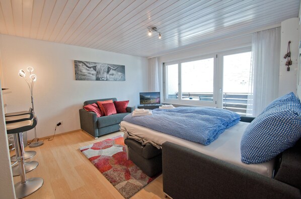 A modern bedroom with a bed, a sofa, a desk, and a window. - Apartment Hirle (Zermatt)
