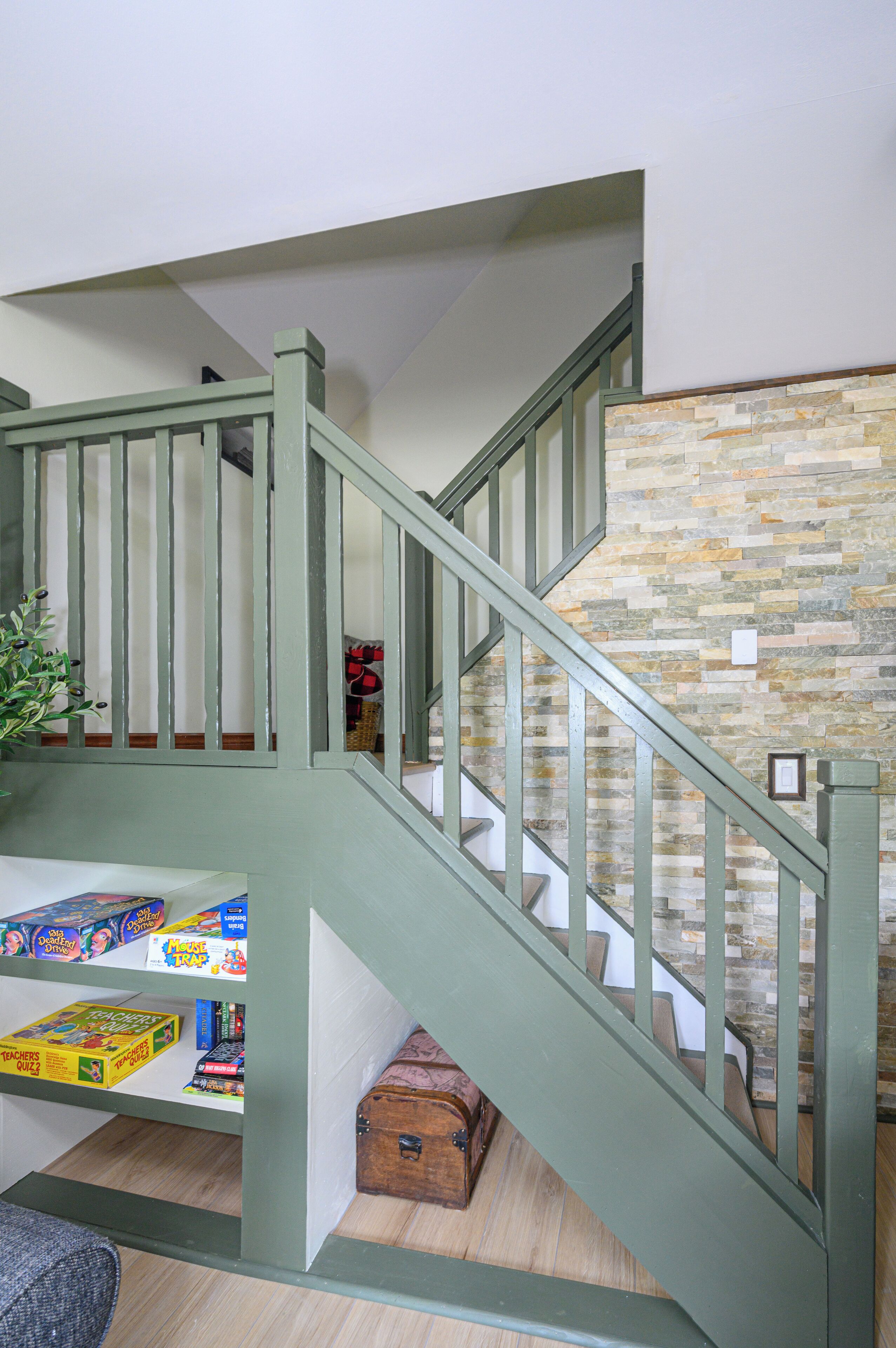 A staircase with green railings, a stone wall, and a wooden chest at the bottom.